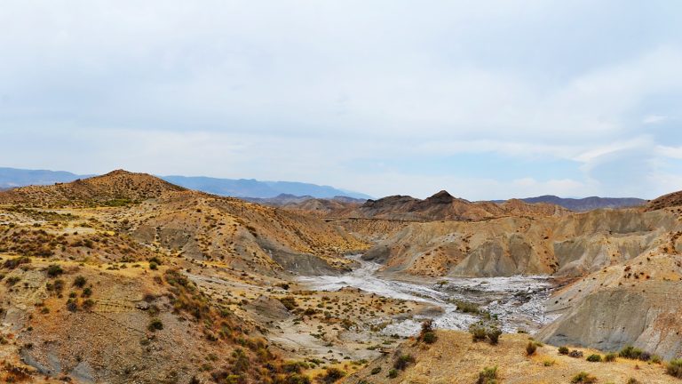 Paysage de badlands arides, collines ocre érodées et ravines sèches sous un ciel voilé