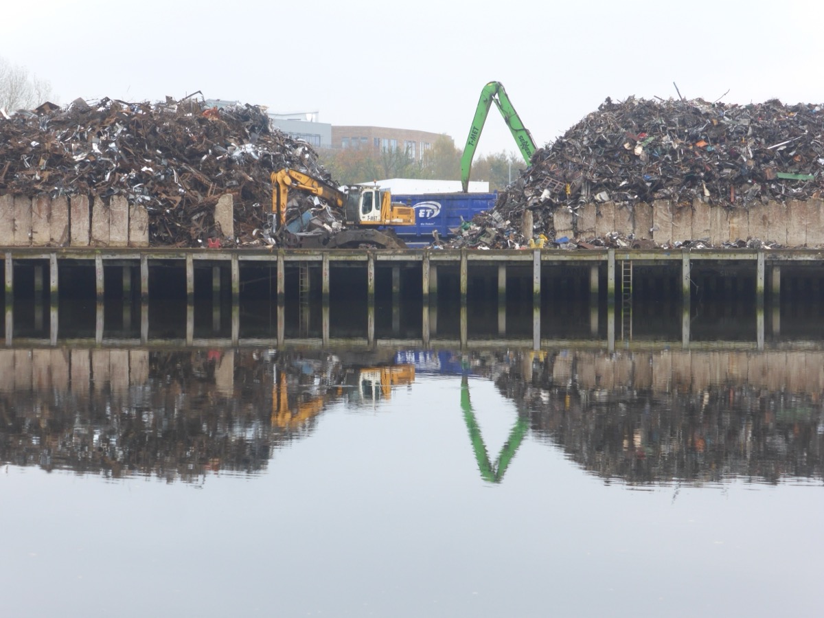 Deux amas de ferrailles séparés par un quai, avec une pelle de manutention et une benne entre les deux.