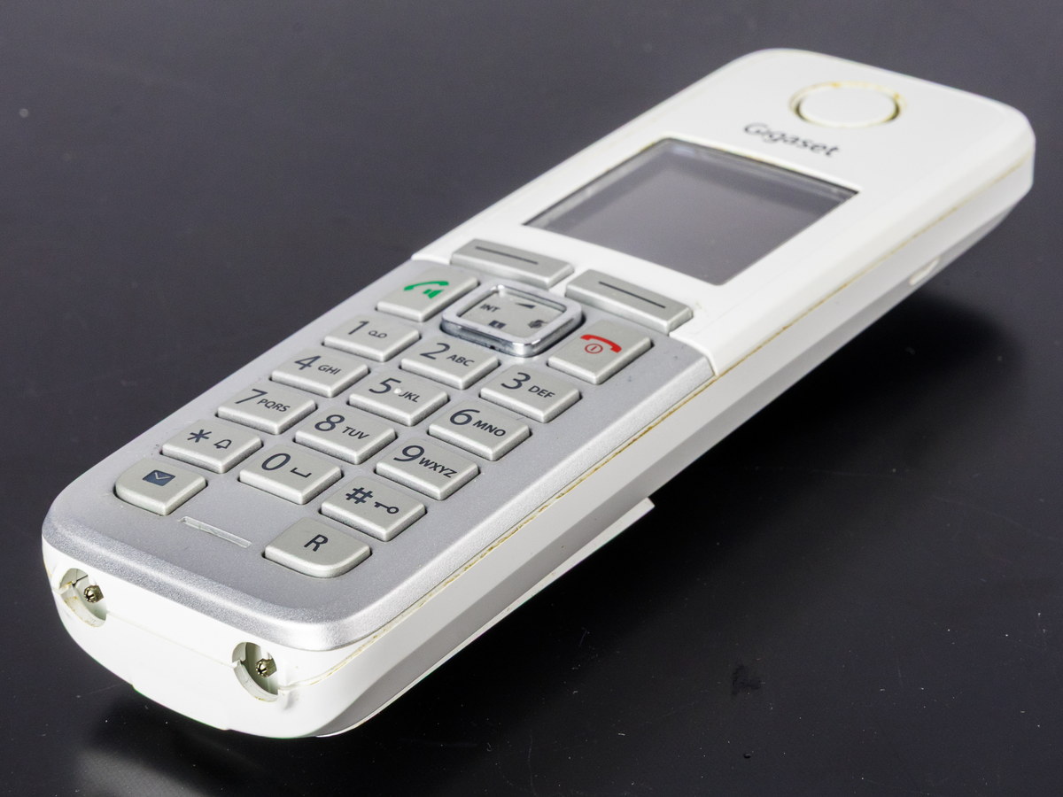 Combiné de téléphone sans fil blanc posé sur une surface sombre, clavier numérique et petit écran visibles