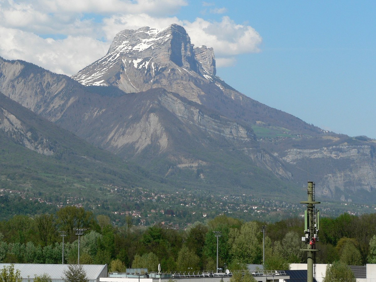 Antenne-relais de téléphonie mobile dressée au-dessus d'une vallée, massif rocheux enneigé à l'arrière-plan