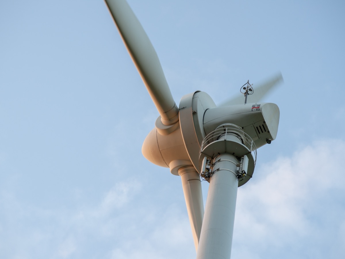 Nacelle d'une éolienne vue en contre-plongée, avec un capteur de vent monté sur le dessus et une pale en rotation