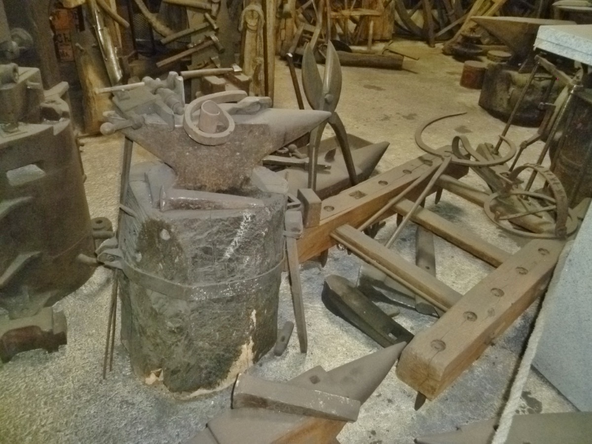 Enclume posée sur un billot de pierre au milieu d’outils de forge, dans un atelier de coutellerie