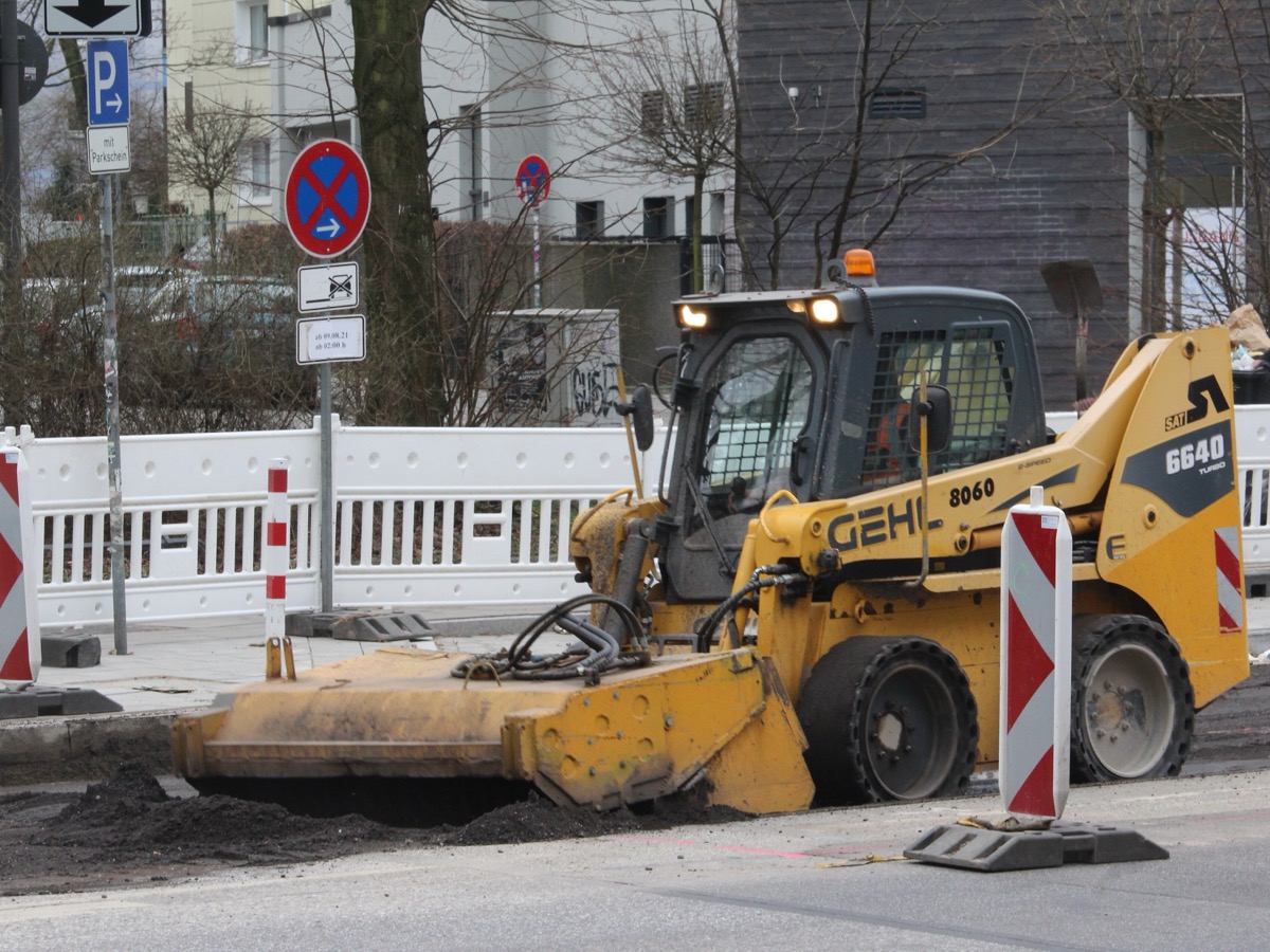 Chargeuse compacte jaune de marque Gehl équipée d'une balayeuse sur une rue en travaux