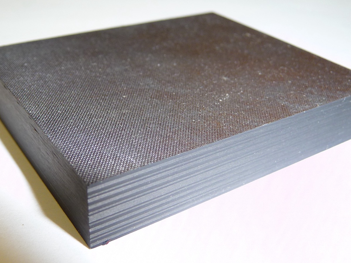 Bloc rectangulaire de stratifié en fibre de carbone posé sur un fond clair, dont la tranche laisse voir les plis superposés