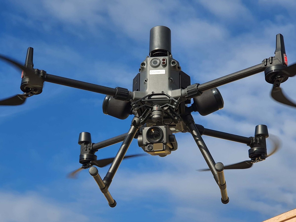 Drone multirotor professionnel en vol, bras en fibre de carbone et nacelle de capteurs sous le fuselage