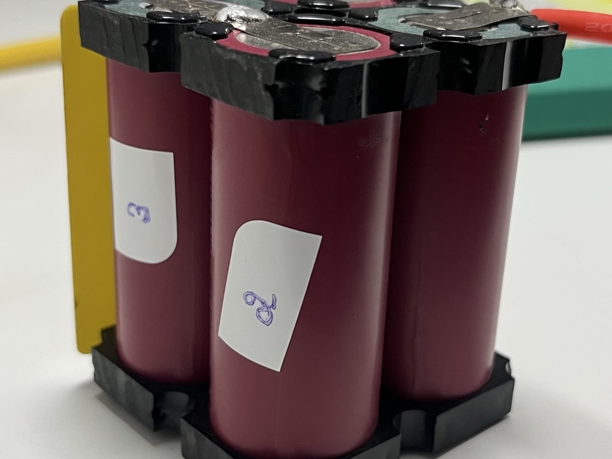Quatre cellules cylindriques de batterie assemblées dans un support noir, posées sur une table