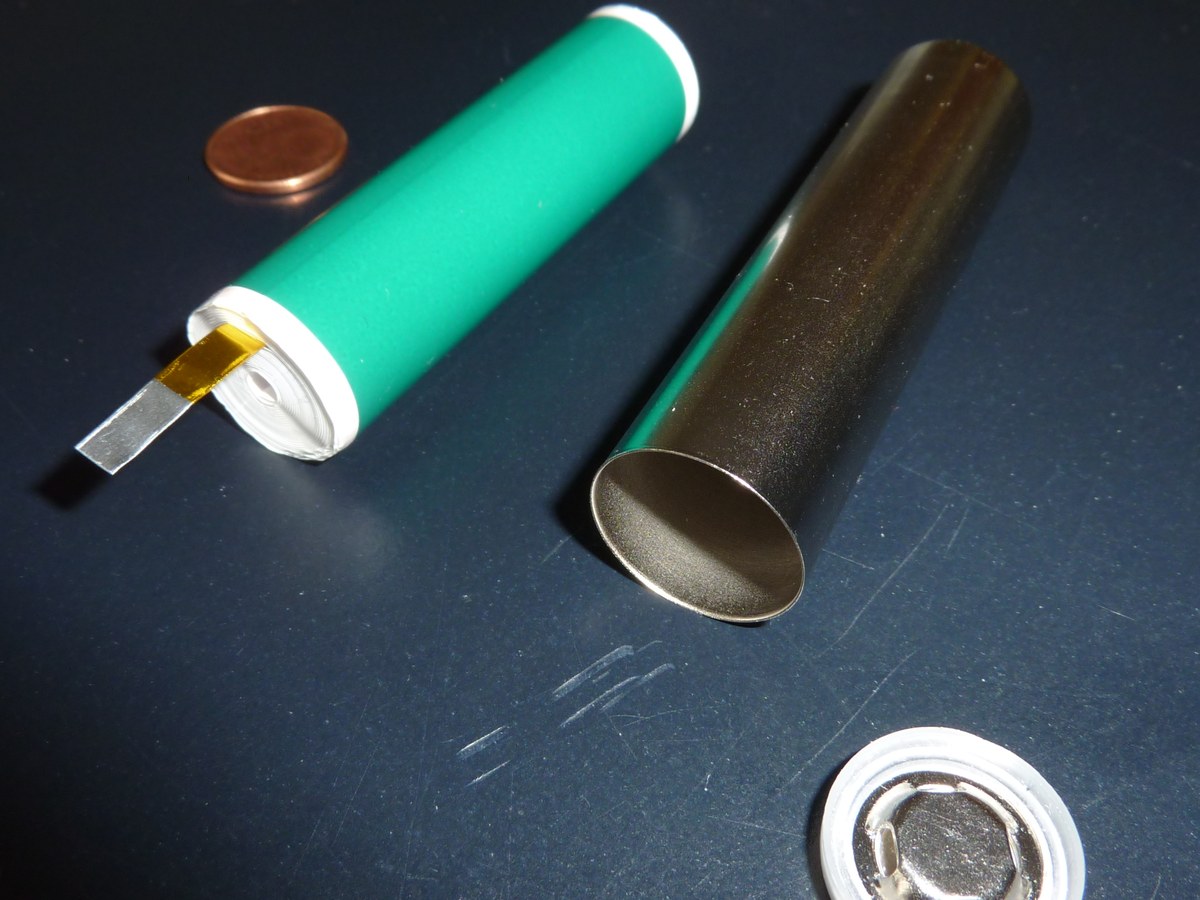 Cellule lithium cylindrique ouverte montrant son enroulement d'électrodes sorti du boîtier métallique, à côté d'une pièce de monnaie