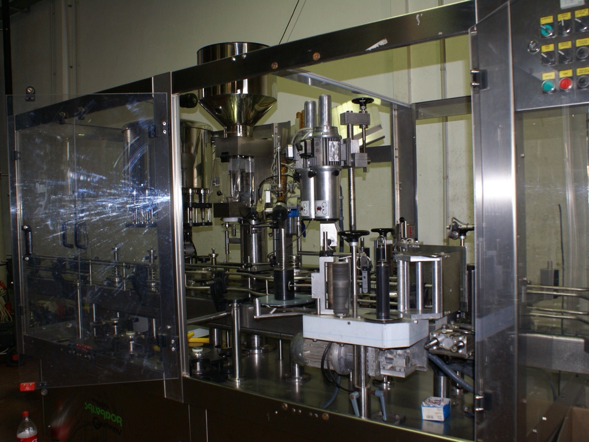 Machine d’embouteillage automatique sous carter transparent, avec armoire de commande et boutons de sécurité, dans un atelier