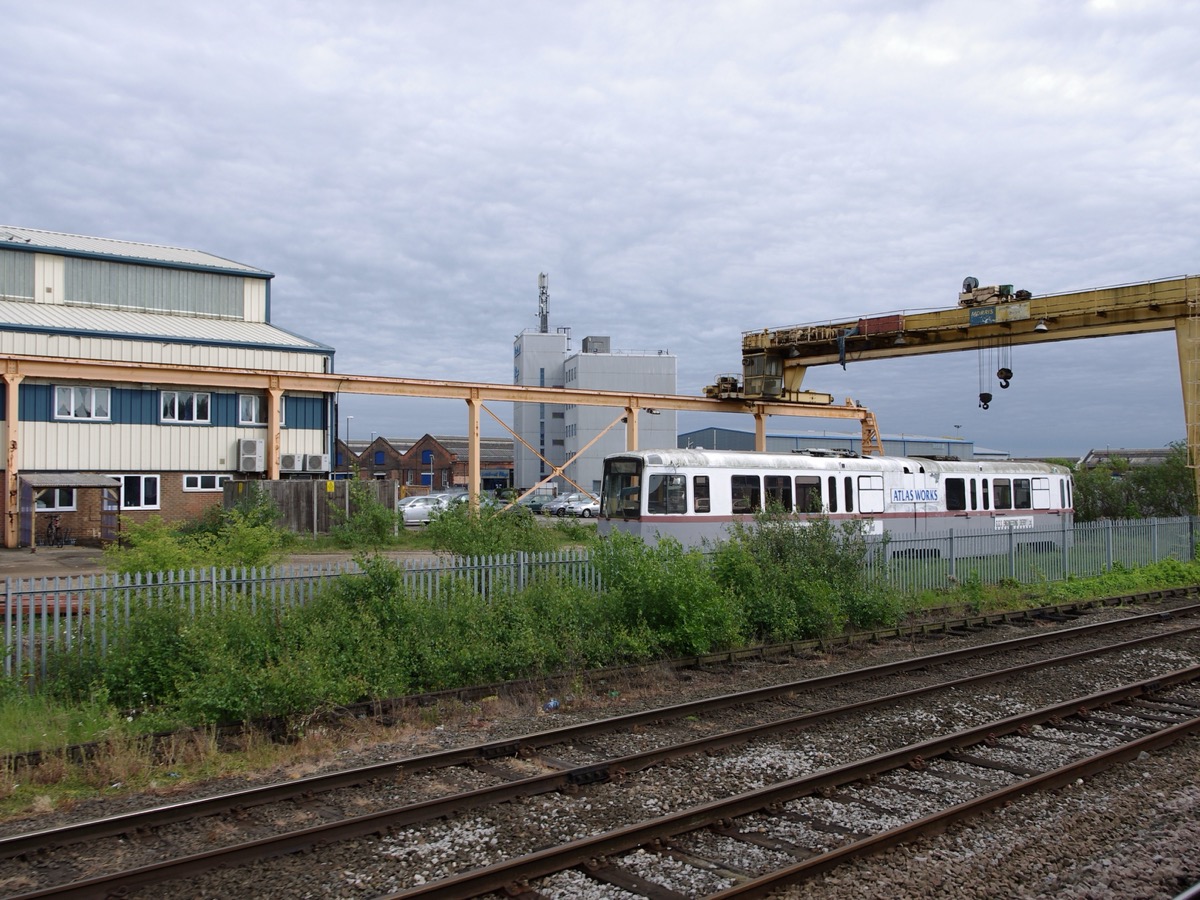 Halle industrielle ferroviaire avec un portique roulant jaune et une rame garée le long des voies