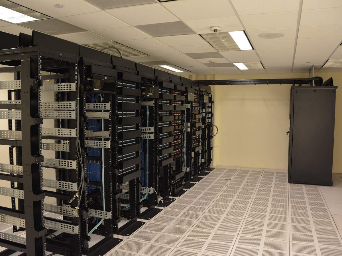 Rangée de baies de serveurs ouvertes et câblées dans une salle informatique au plancher technique perforé
