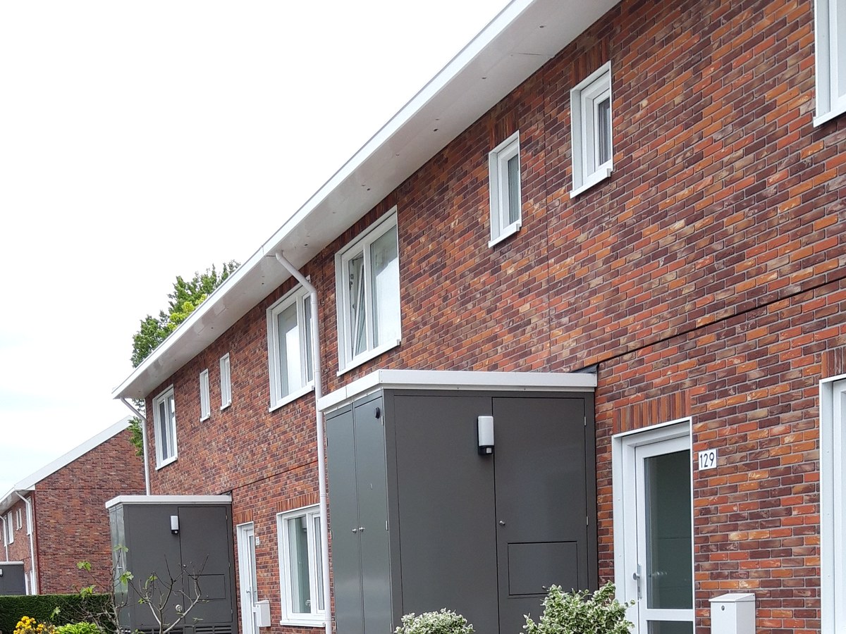 Rangée de maisons mitoyennes en brique devant lesquelles sont installés des coffrets gris abritant des pompes à chaleur