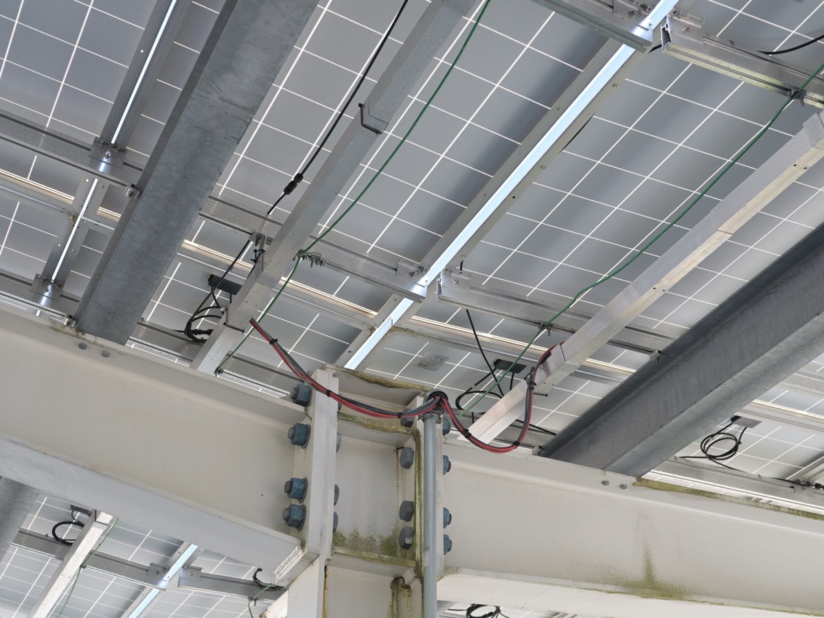 Dessous d’une ombrière de parking montrant les cellules des modules photovoltaïques, les rails de fixation et les câbles