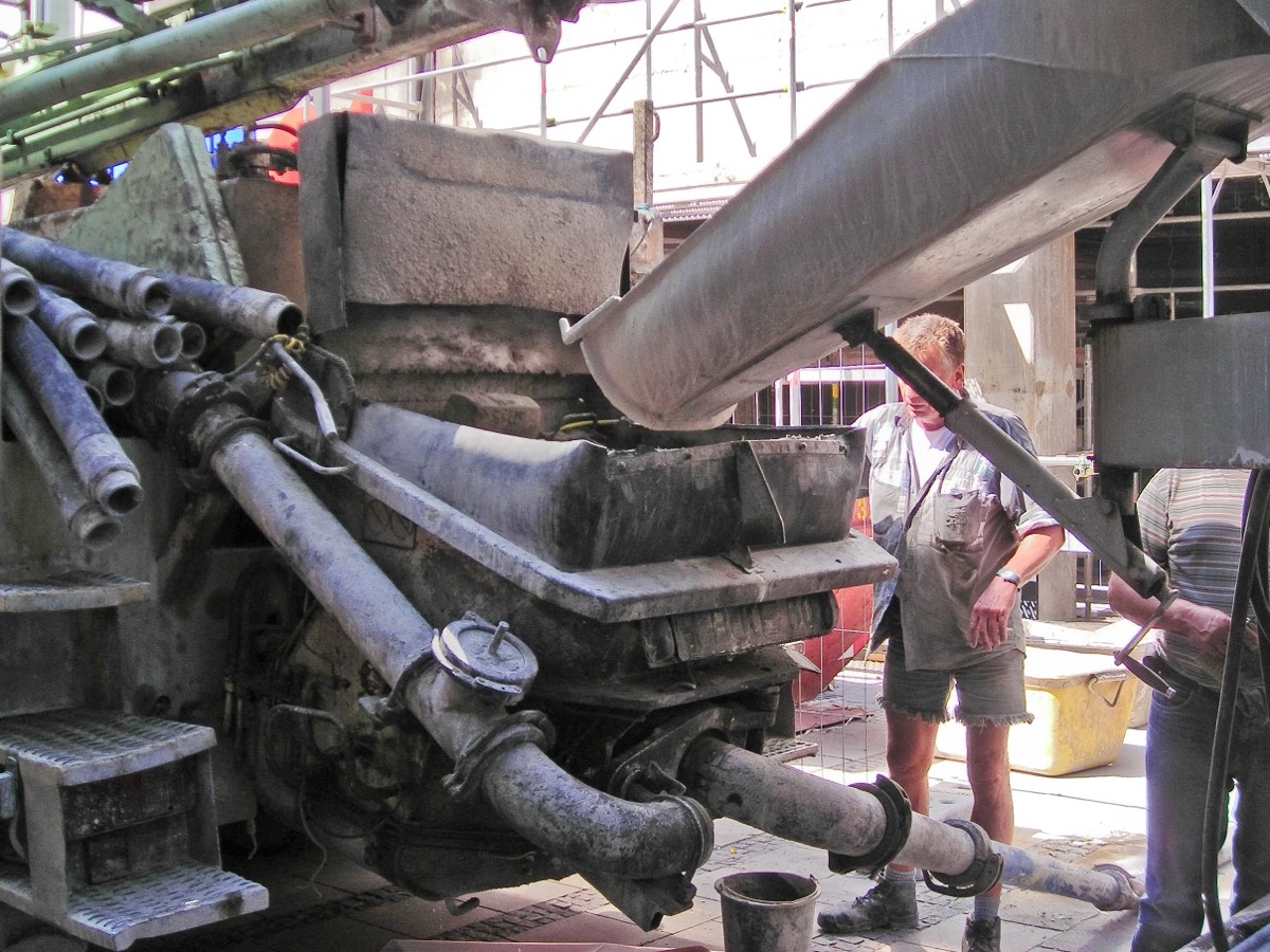 Goulotte d’un camion malaxeur déversant du béton frais dans la trémie d’une pompe à béton, sur un chantier