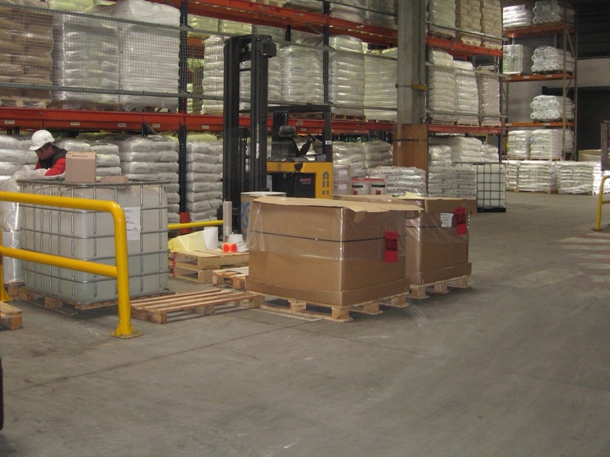 Rayonnages à palettes chargés de sacs et de cartons dans un entrepôt de matières premières, avec un chariot élévateur