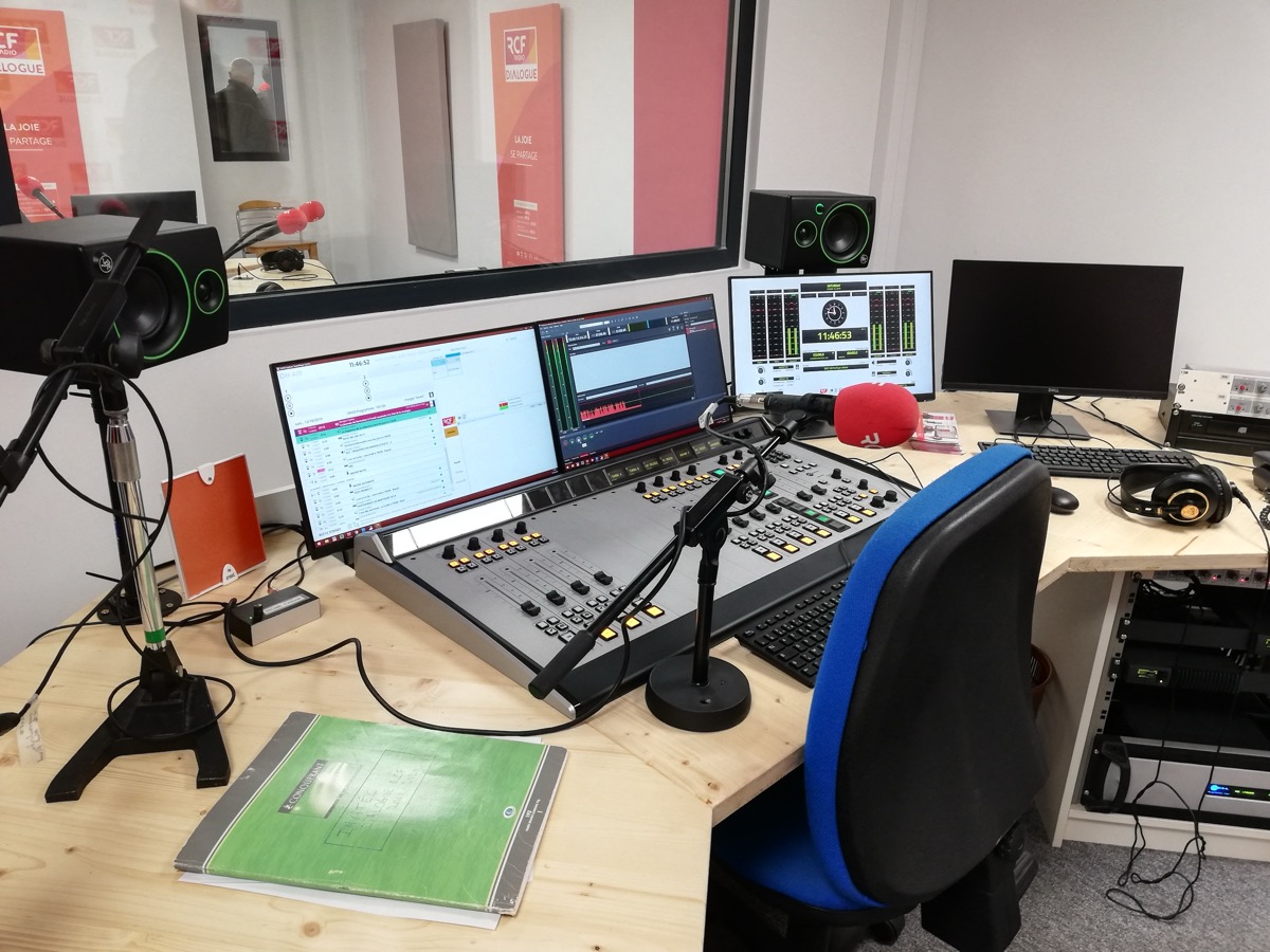 Régie d'une station de radio avec console de mixage, micro rouge, écrans de programmation et baie technique