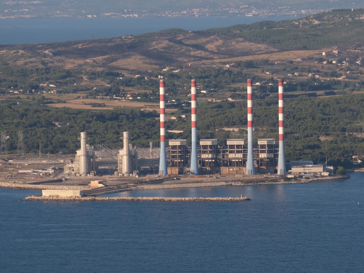 Centrale thermique en bord de mer avec deux cheminées grises et quatre cheminées bleues, rouges et blanches