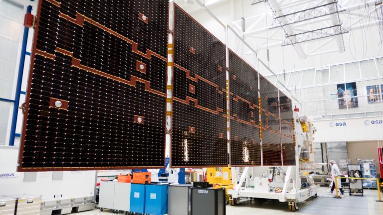Aile solaire du satellite EarthCARE entièrement déployée dans une salle d'essais, à côté du corps du satellite