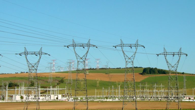 Alignement de pylônes à haute tension au-dessus d'un poste électrique, dans une campagne vallonnée