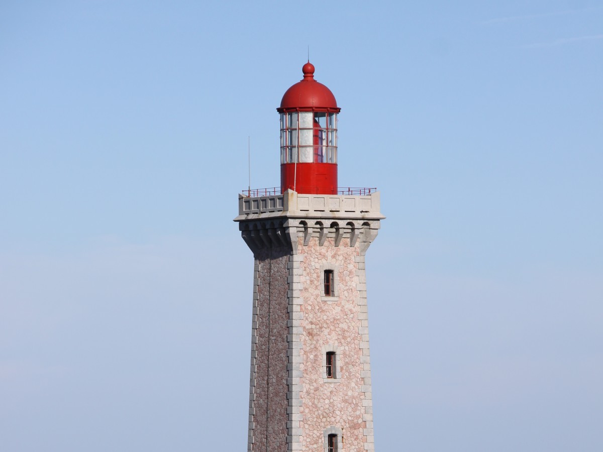Haut d un phare de pierre claire coiffe d une lanterne rouge, sur fond de ciel