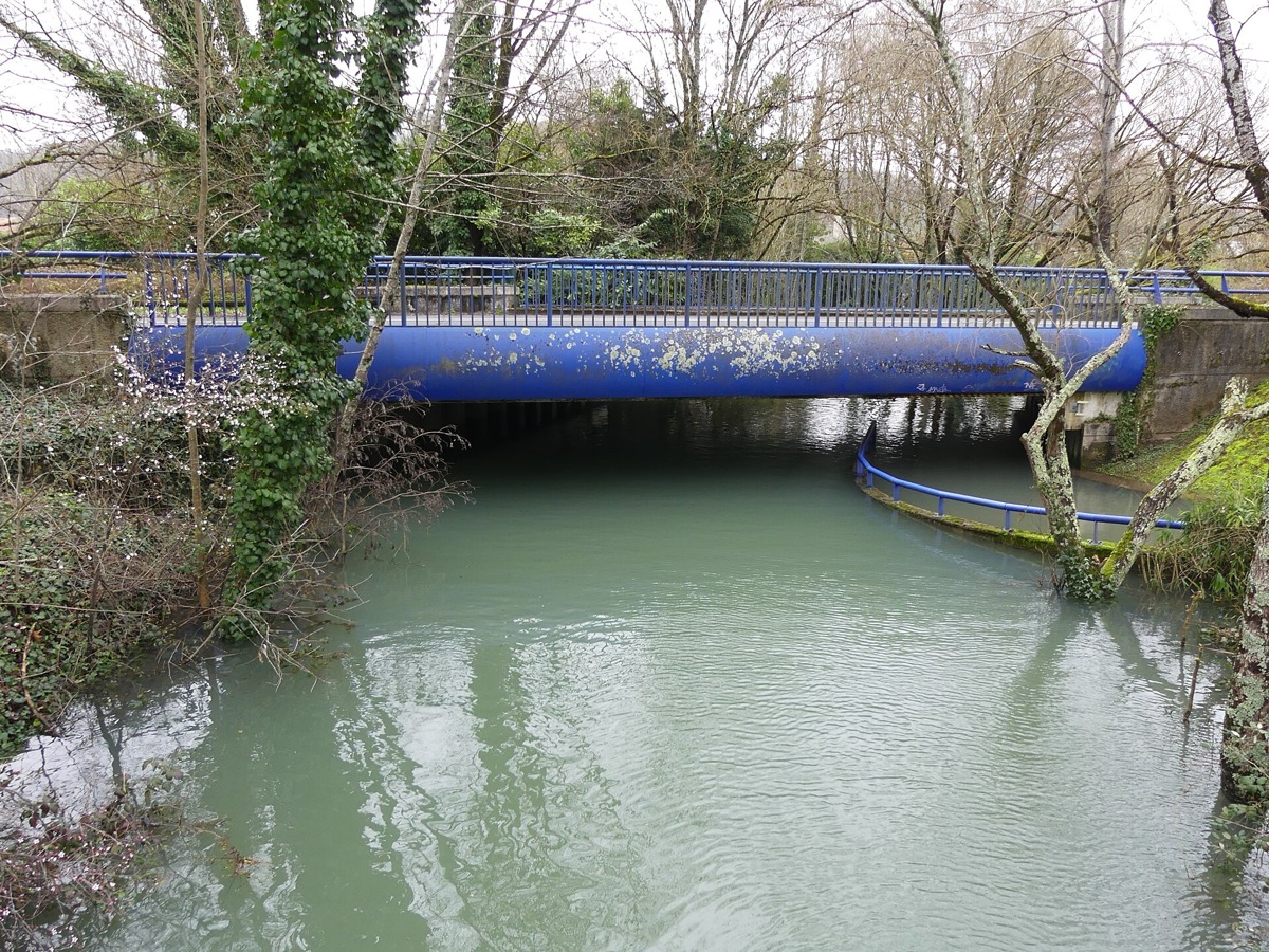 Un petit cours d'eau sorti de son lit sous un pont bleu, la rambarde d'une passerelle à demi noyée