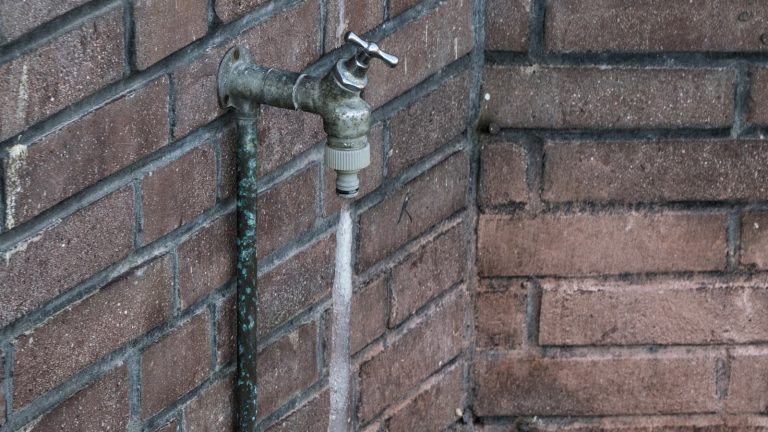 Robinet extérieur en laiton fixé sur un mur de brique, prolongé par une longue stalactite de glace