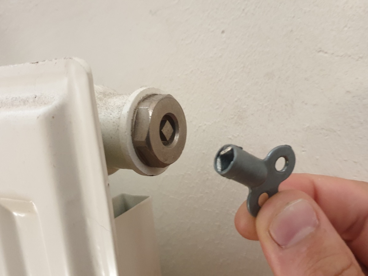 Main tenant une clé de purge devant le robinet de purge situé en haut d'un radiateur blanc