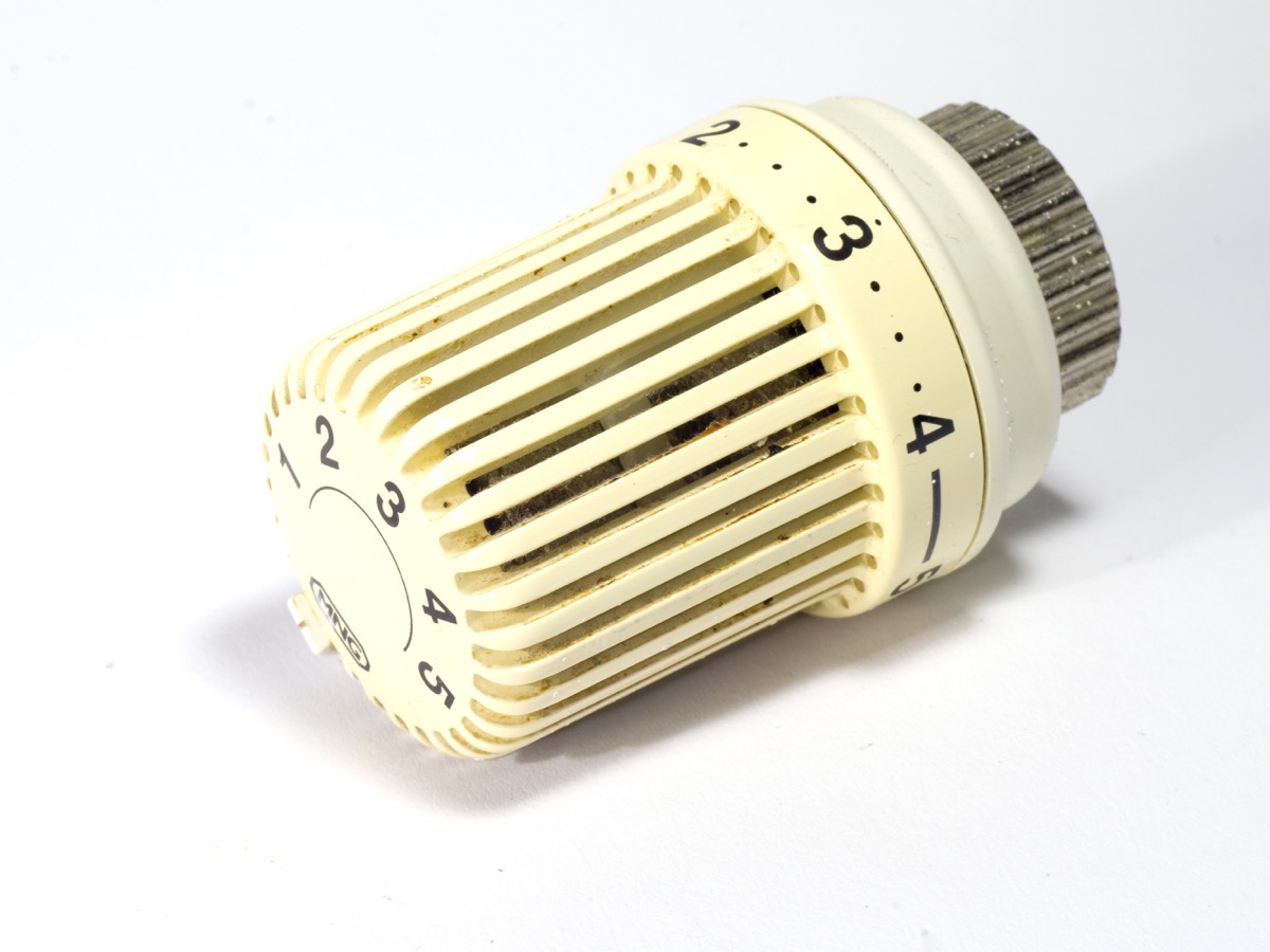 Tête thermostatique de radiateur posée sur un fond clair, graduée de 1 à 5