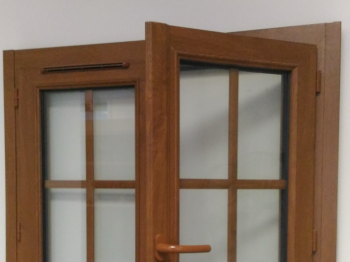 Fenêtre PVC à deux vantaux entrouverte, avec une entrée d'air en traverse haute et les paumelles visibles