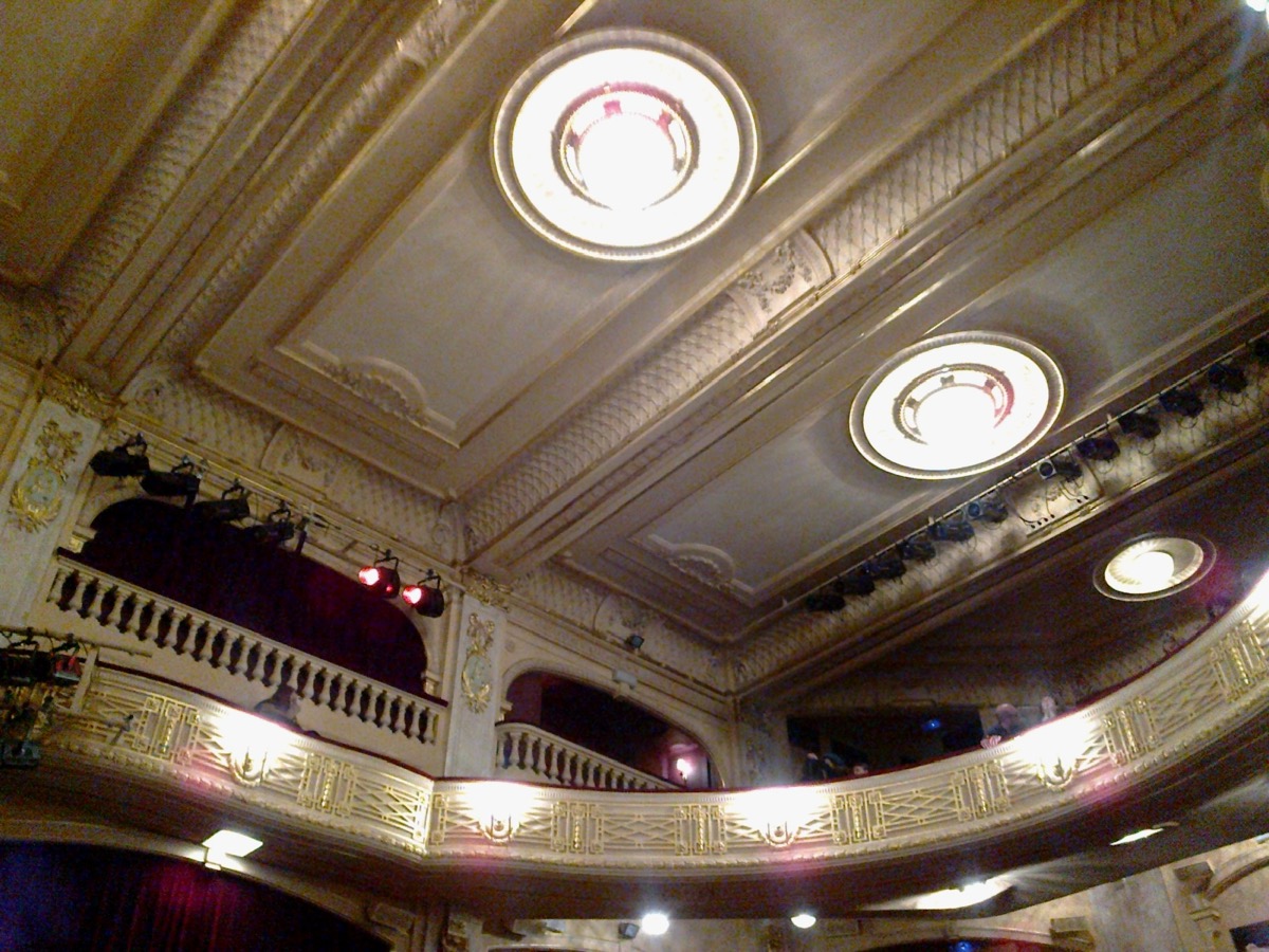 Plafond à caissons et balcons dorés d'une salle de théâtre, avec des projecteurs accrochés à la rambarde du premier balcon