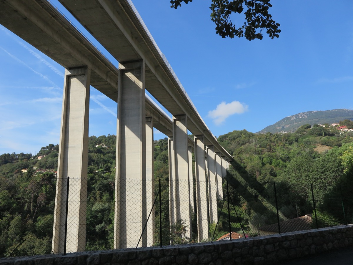 Viaduc en béton d’autoroute franchissant un vallon boisé, au-dessus d’un grillage et d’un muret de pierre