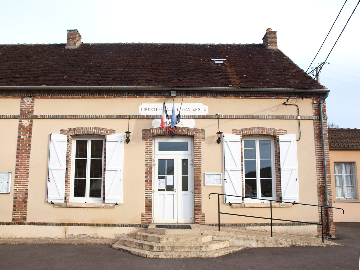 Façade d'une mairie-école de village avec la devise républicaine gravée au-dessus de la porte et des volets blancs