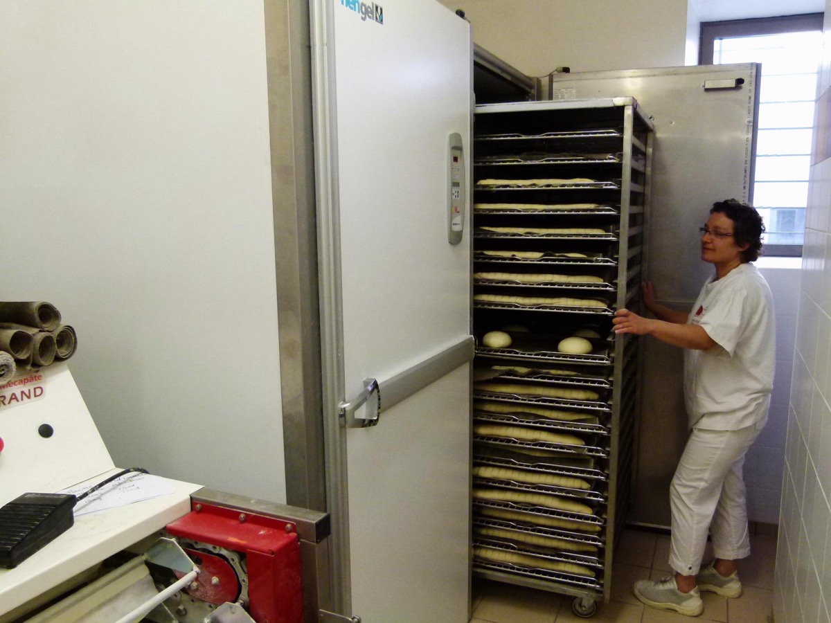 Une boulangère pousse une échelle chargée de pâtons dans une chambre de pousse d'un fournil