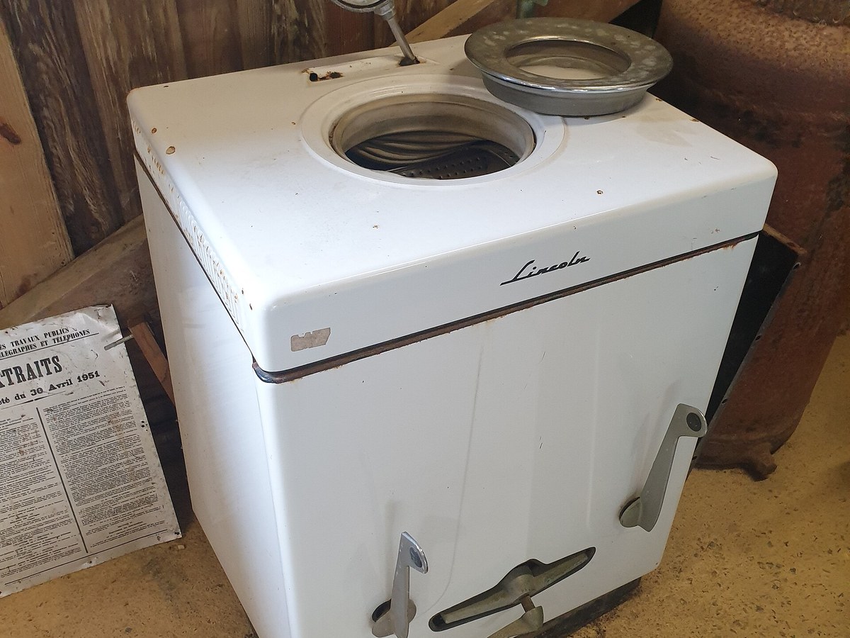 Machine à laver blanche à cuve ronde, posée dans une salle d'exposition en bois, avec un thermomètre sur le couvercle