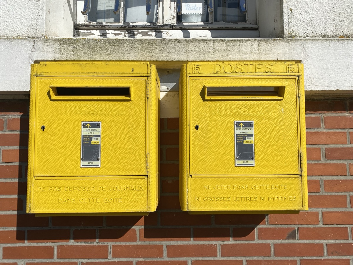 Deux boîtes aux lettres jaunes de La Poste fixées côte à côte sur un mur de briques, avec leurs étiquettes de levée
