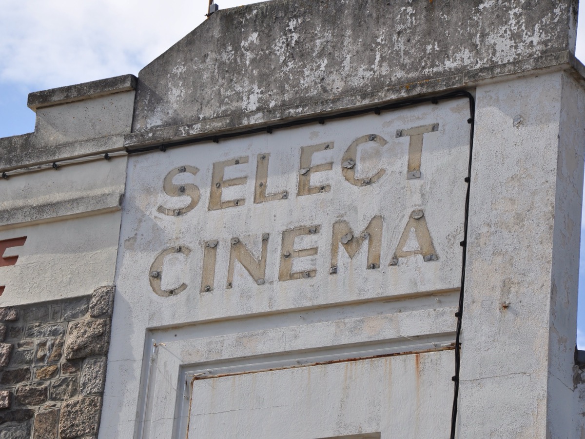 Fronton d'un ancien cinéma de bord de mer, lettres en relief formant le mot cinéma sur un enduit blanc usé