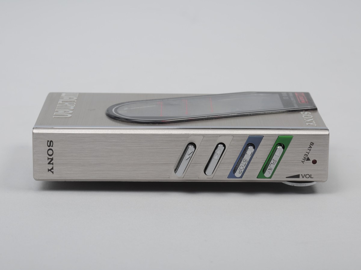Baladeur à cassette Sony vu de profil sur fond gris, avec ses touches de commande, la molette de volume et le témoin de pile