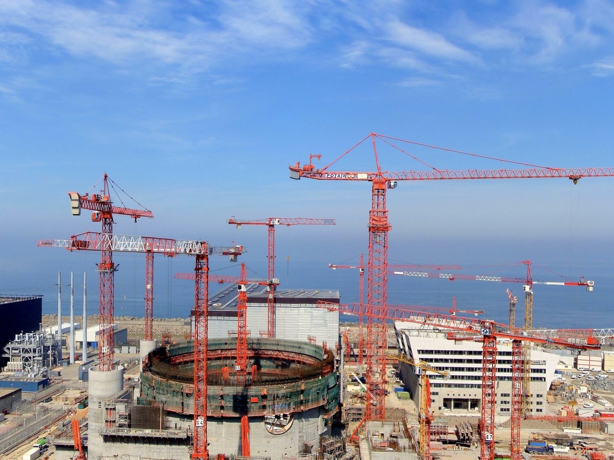 Grues de chantier rouges autour d’un bâtiment circulaire en construction sur le site nucléaire de Flamanville, au bord de la mer